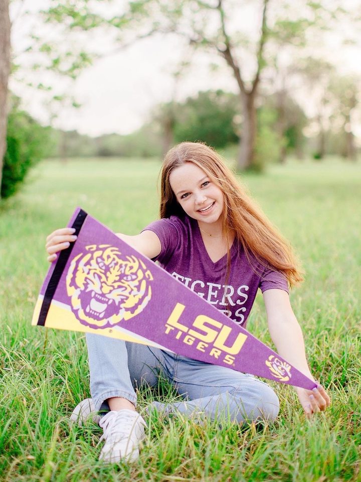 A high school senior holding an LSU Tigers pennant in a field